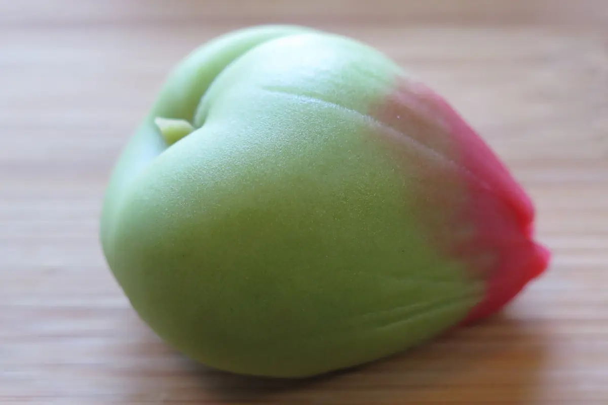 Bledě žlutý wagashi cukroví ve tvaru květiny s hnědým středem a zeleným lístkem na dřevěném stole