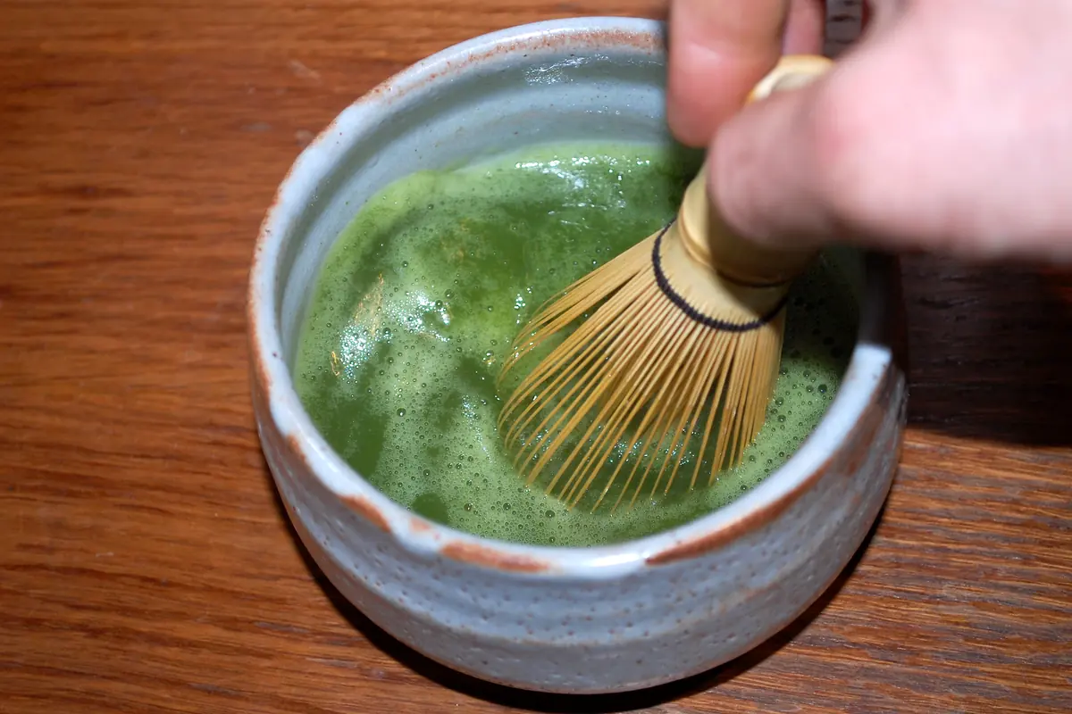 一只手在盛满泡沫抹茶的碗中搅动竹制茶筅